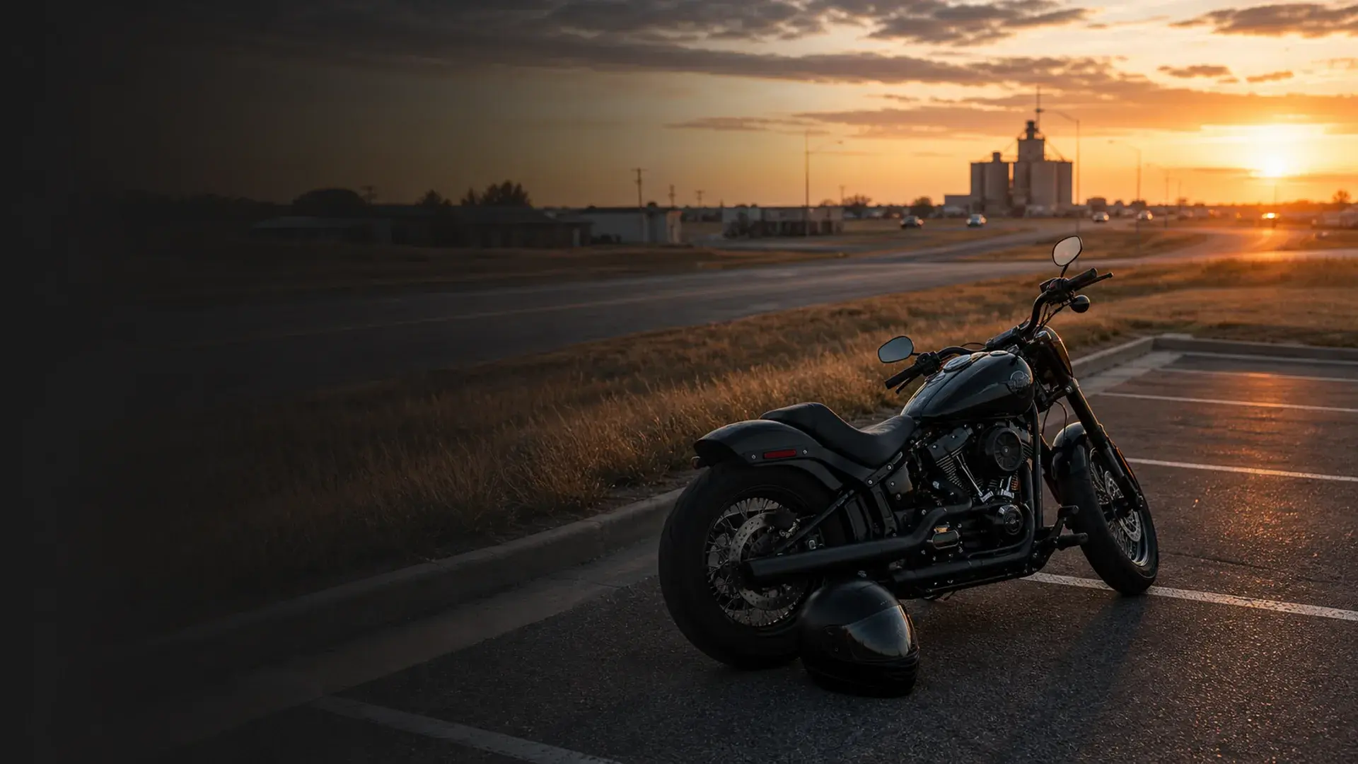 Motorcycle parked safely near an Enid plains highway with grain-elevator silhouette and sunset sky